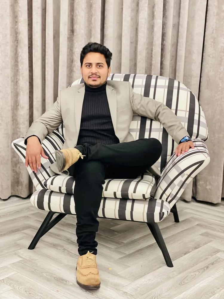 Shanawar in a blazer seated in a lounge chair